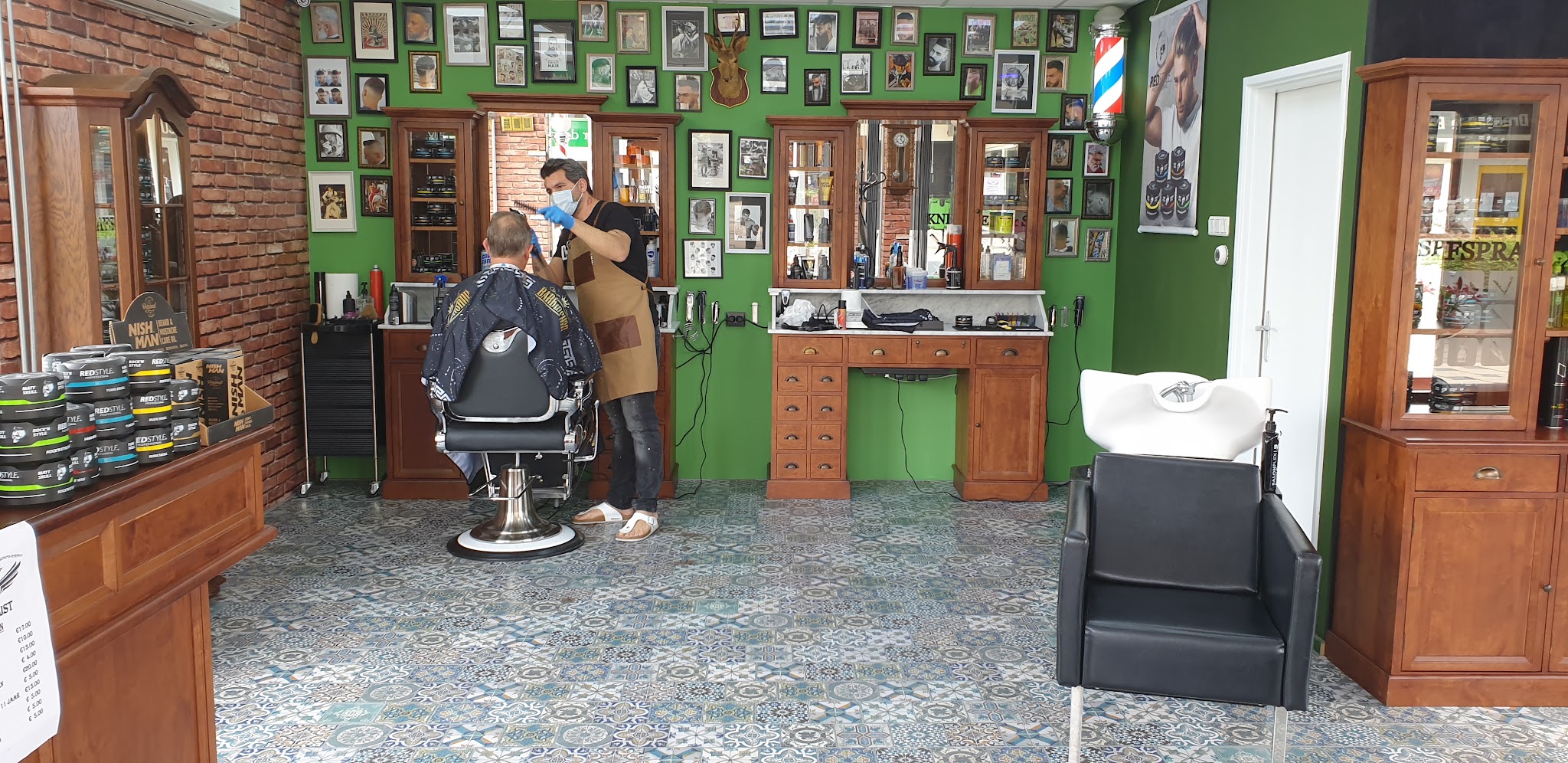 Het interieur van Kapsalon Hoogeveen met de groene wand vol ingelijste foto's, een kappersstoel en de houten kasten