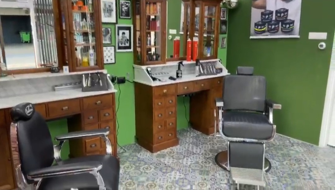 Twee kappersstoelen voor de houten werkplekken met spiegels, tegen de groene wand